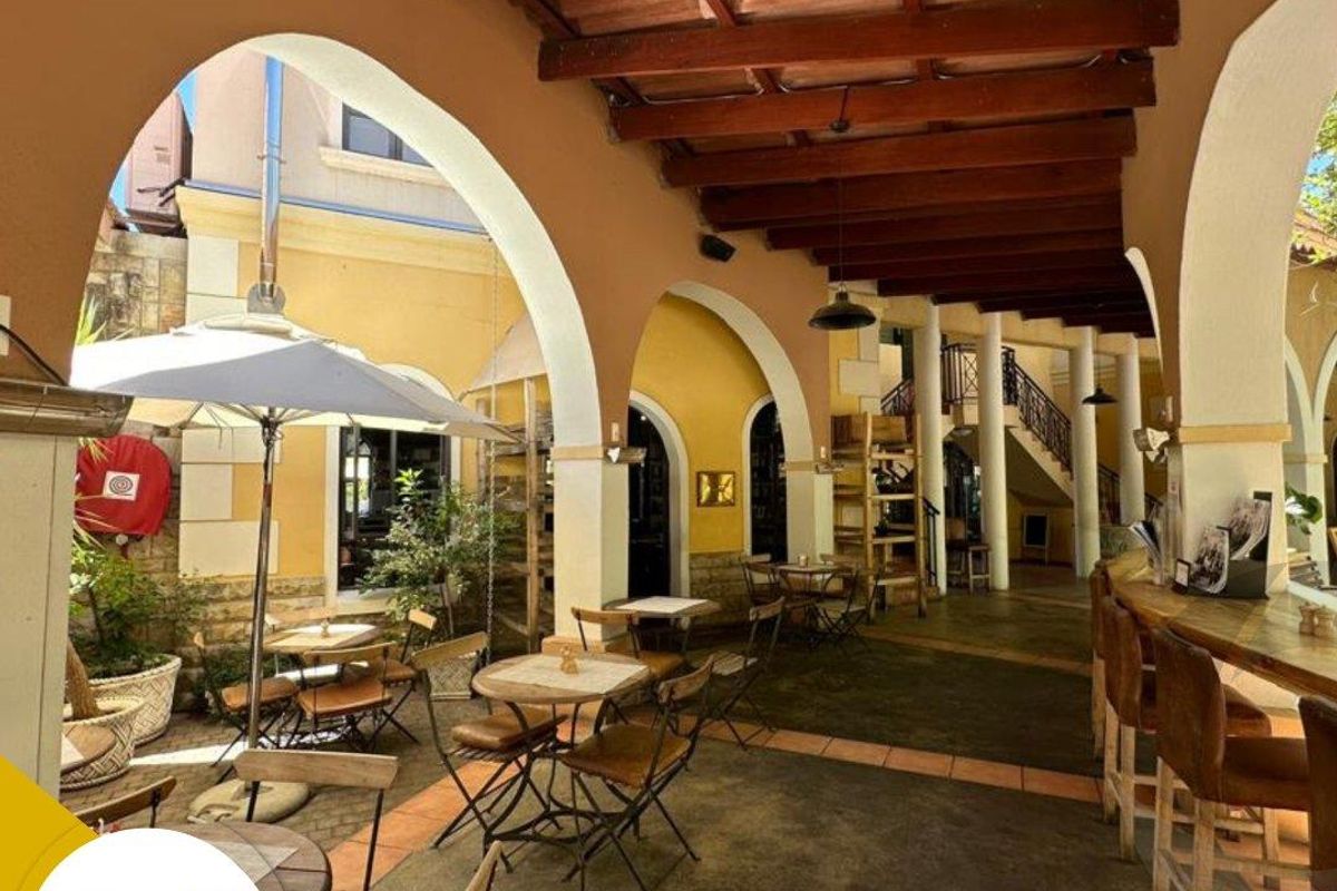 A spacious covered outdoor patio featuring exposed timber beams, arched architectural columns, and a built-in bar area, ideal for office breakout or social space.