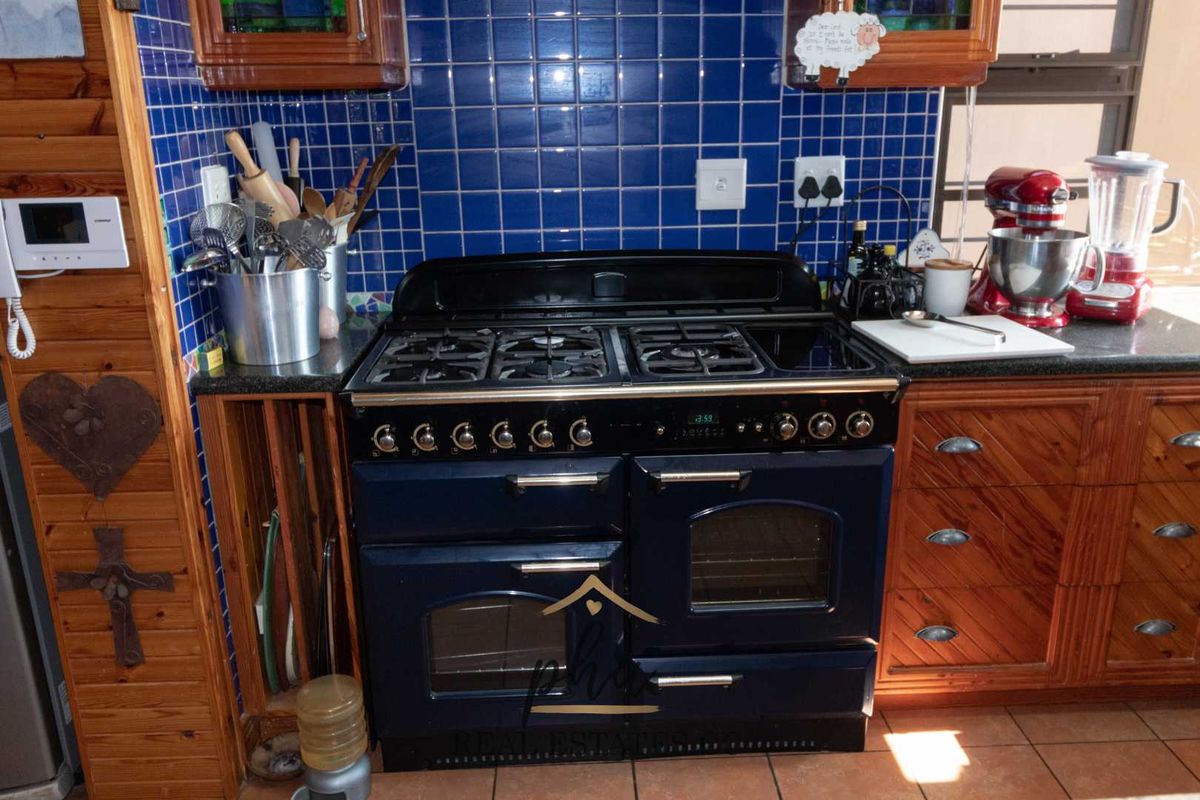 A kitchen featuring a large dark blue freestanding gas range, granite countertops, and blue tiled backsplash with traditional wooden cabinetry.