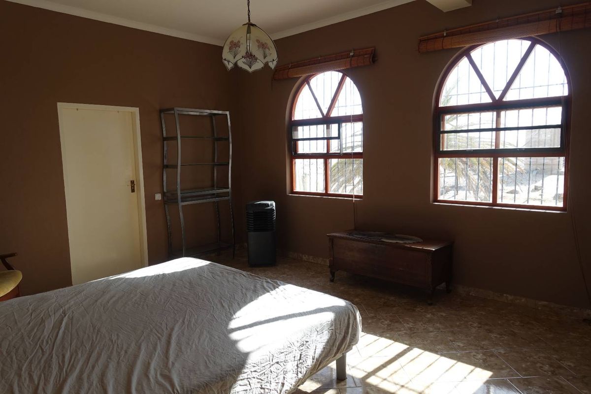 A bedroom featuring arched windows with security bars, tiled flooring, and neutral wall tones, offering a functional and well-lit living space.