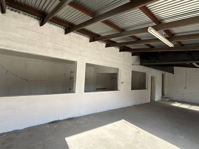 Spacious industrial utility area featuring exposed steel roof trusses, corrugated metal ceiling, painted masonry walls, and durable concrete flooring.