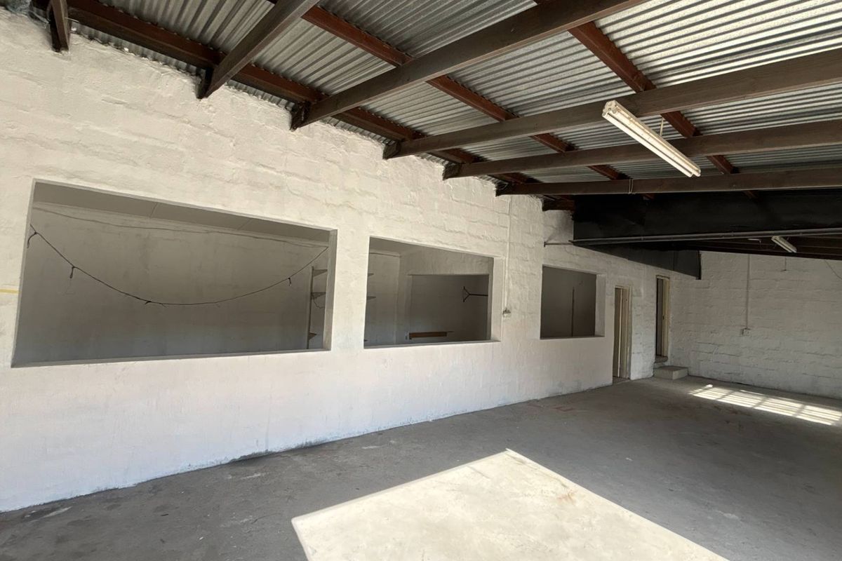 Spacious industrial utility area featuring exposed steel roof trusses, corrugated metal ceiling, painted masonry walls, and durable concrete flooring.