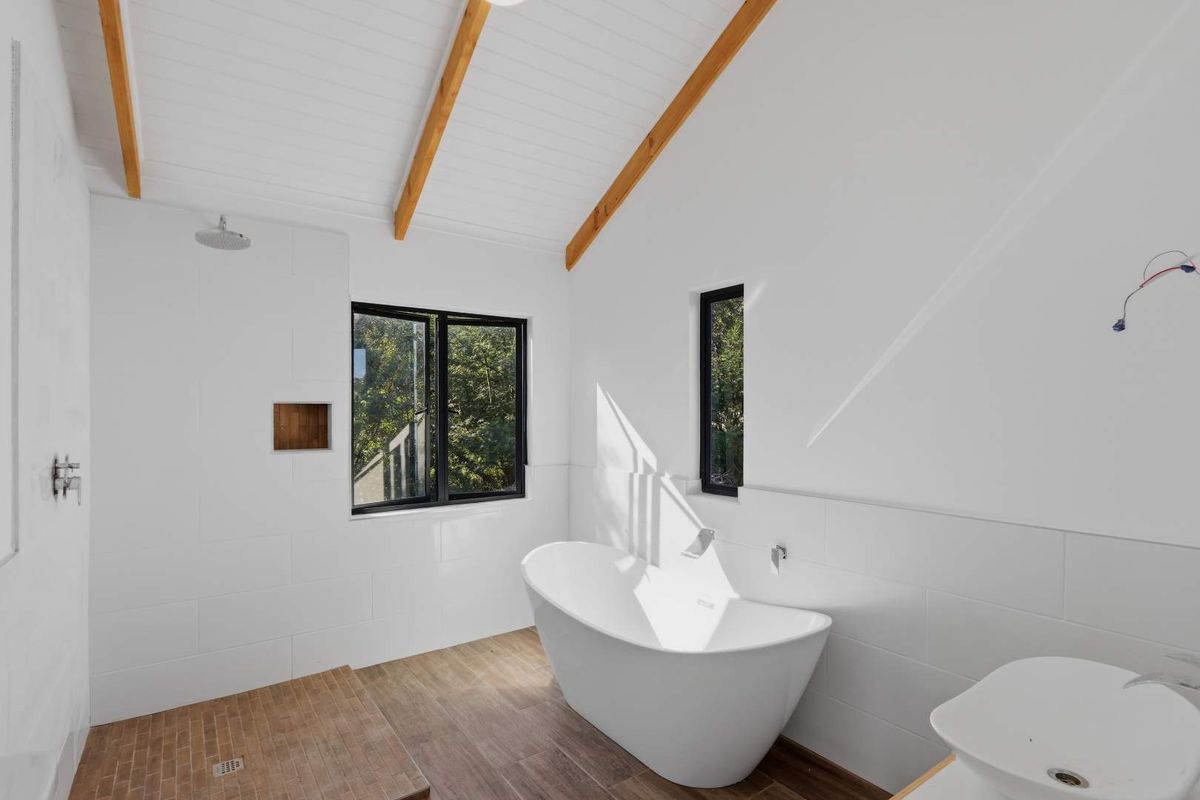 Modern bathroom featuring a freestanding bathtub, walk-in shower area, timber-look flooring, and vaulted ceilings with exposed wooden beams.