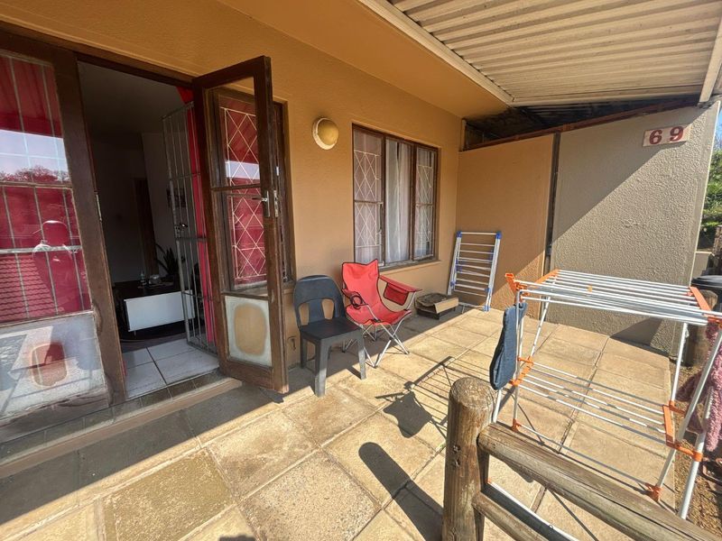 A covered outdoor patio area featuring tiled flooring, a corrugated roof, and direct access to the interior through a security gate and timber door.