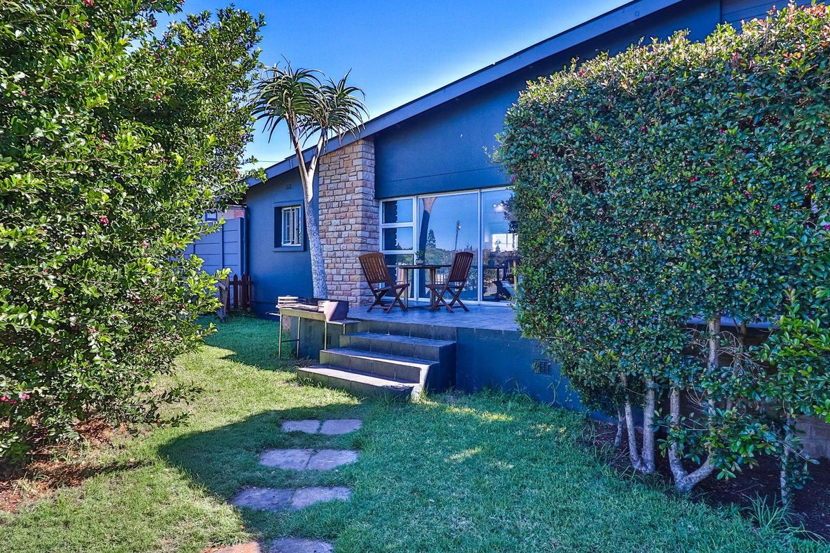 A rear exterior view featuring a paved patio area, stone-clad wall accents, and sliding glass doors leading into the home, set within a landscaped garden.