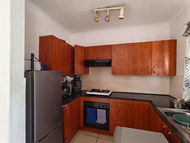 A functional kitchen featuring wooden cabinetry, black granite countertops, a built-in oven with gas hob, and a tiled backsplash.
