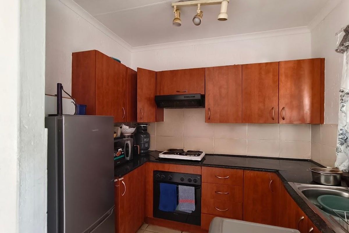 A functional kitchen featuring wooden cabinetry, black granite countertops, a built-in oven with gas hob, and a tiled backsplash.