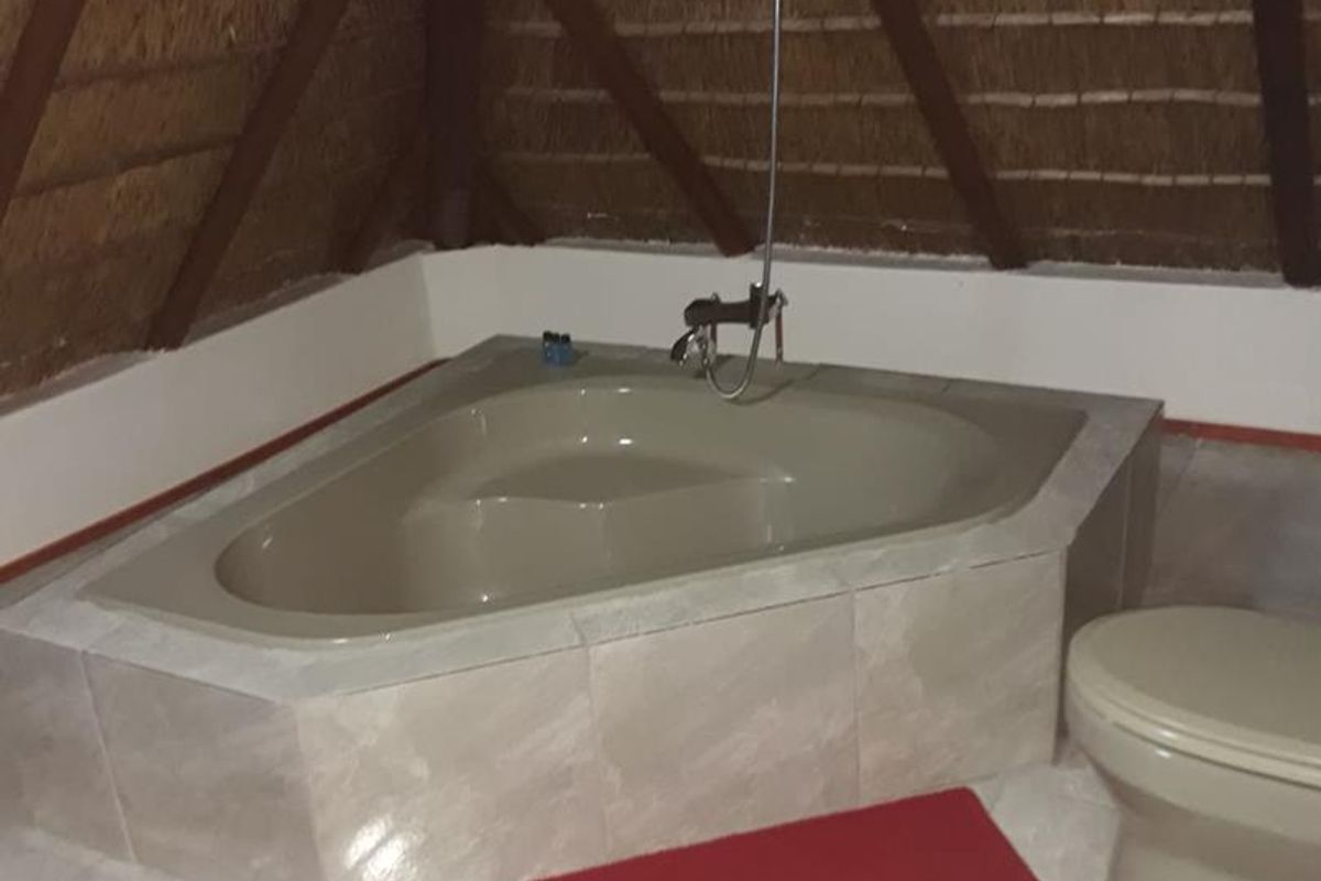 A bathroom featuring a corner bathtub with a shower attachment, set under a traditional thatched roof with exposed timber beams.