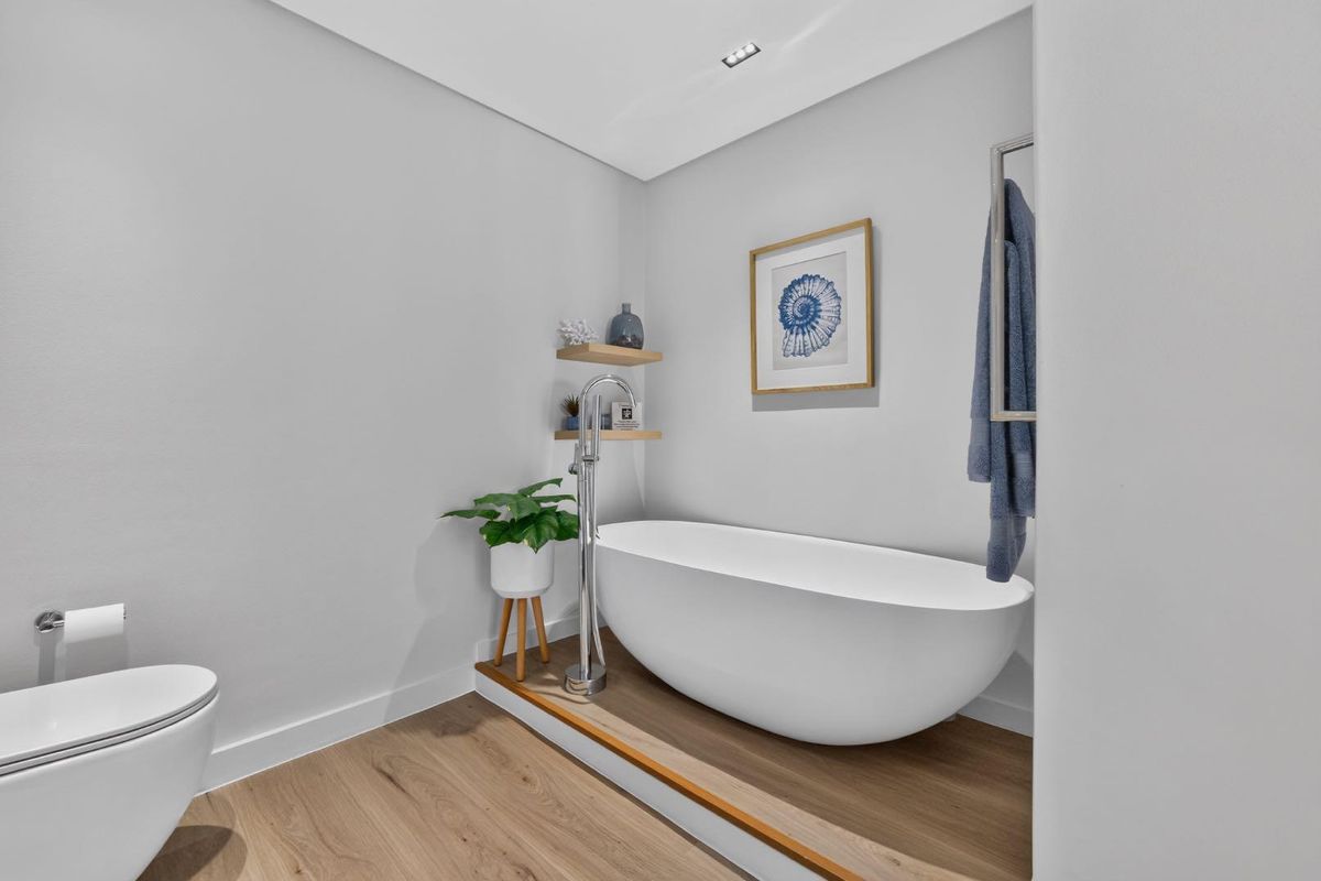 Modern bathroom featuring a sleek freestanding bathtub with floor-mounted faucet, wall-hung toilet, and contemporary timber-look flooring.