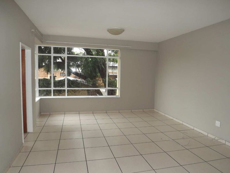 A bright, empty living room featuring neutral tiled flooring, a large multi-pane window, and a simple ceiling light fixture.