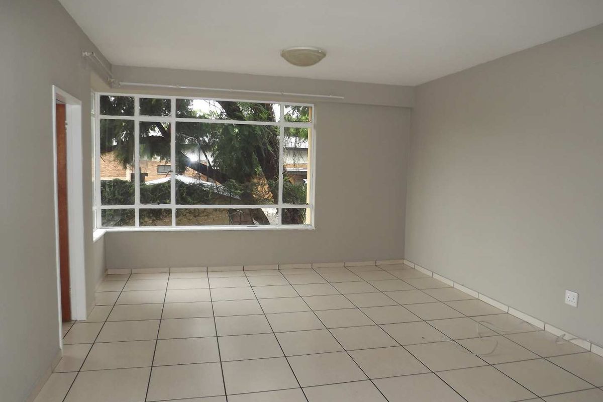 A bright, empty living room featuring neutral tiled flooring, a large multi-pane window, and a simple ceiling light fixture.