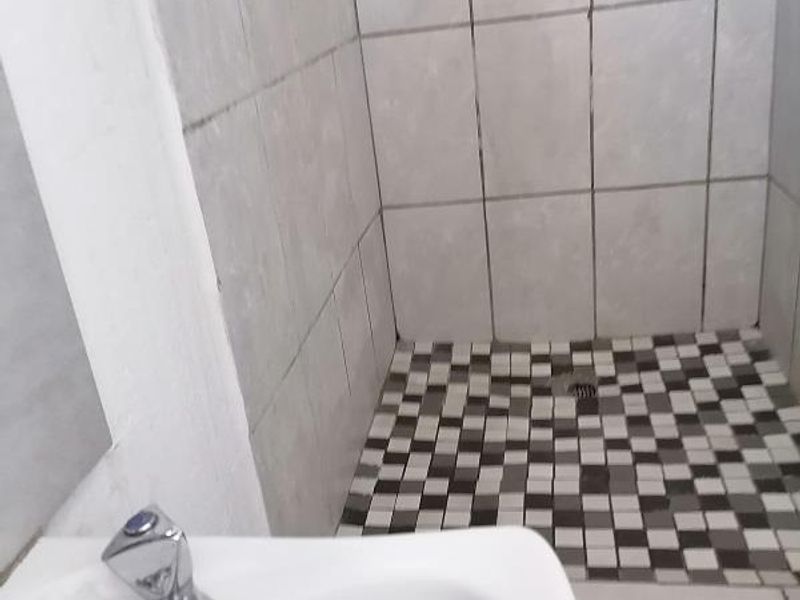 A functional bathroom space featuring a tiled shower enclosure with mosaic flooring and a modern basin with a chrome mixer tap.