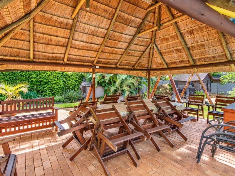 Covered outdoor patio area featuring a traditional thatched roof, timber support structure, and brick paved flooring, ideal for outdoor entertaining.