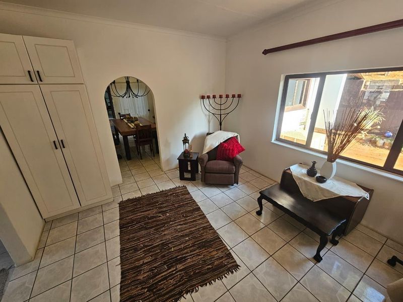 A living area featuring ceramic floor tiles, built-in cabinetry, and an arched doorway leading to the dining space.