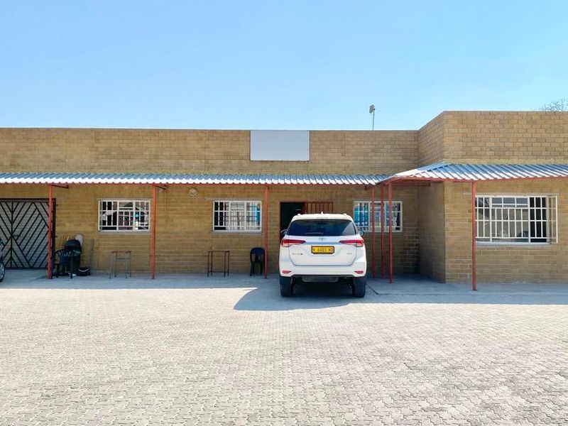 Front elevation of a commercial building featuring a face brick facade, corrugated metal roof canopy, and a paved parking area.
