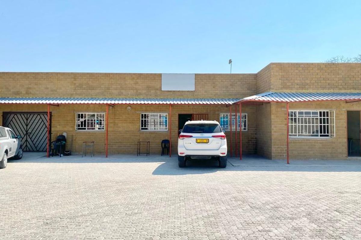 Front elevation of a commercial building featuring a face brick facade, corrugated metal roof canopy, and a paved parking area.