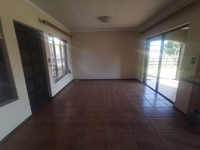 An empty, open-plan living area featuring tiled flooring, large sliding glass doors leading to the exterior, and neutral wall finishes.