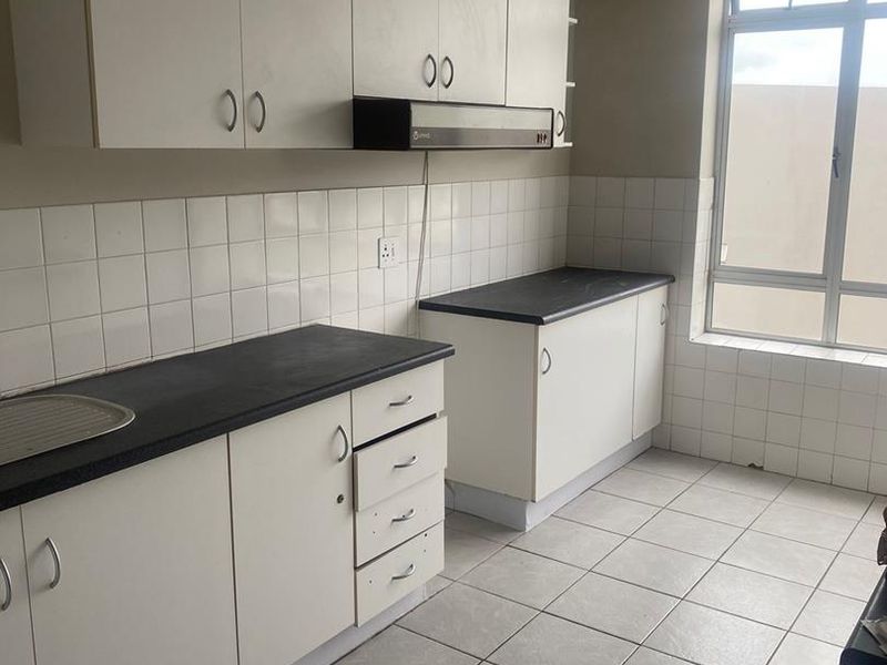 A functional, empty kitchen featuring white cabinetry, dark laminate countertops, tiled backsplash, and tiled flooring, offering a clean canvas for potential updates.
