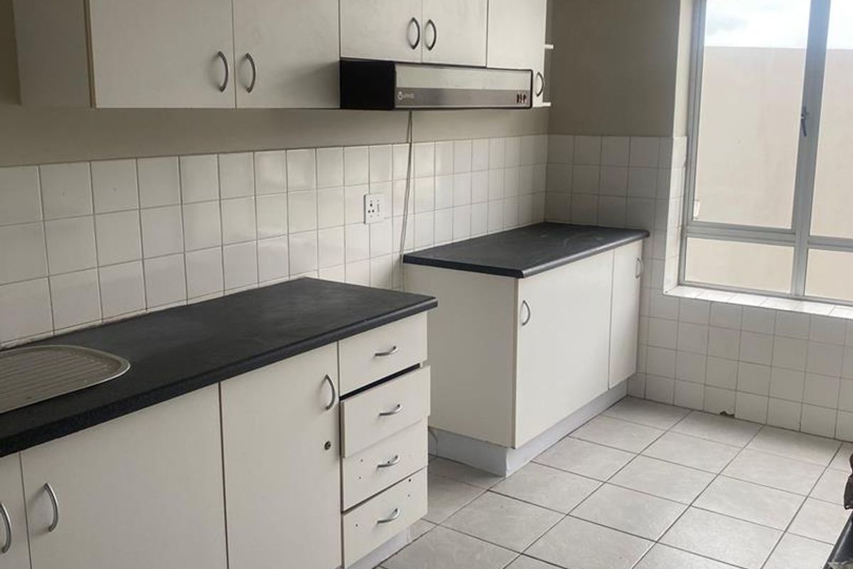 A functional, empty kitchen featuring white cabinetry, dark laminate countertops, tiled backsplash, and tiled flooring, offering a clean canvas for potential updates.