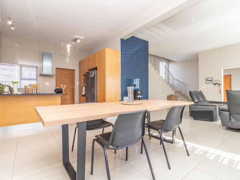 Open-plan living and dining area featuring a modern kitchen with built-in cabinetry, tiled floors, and a staircase with a metal balustrade.