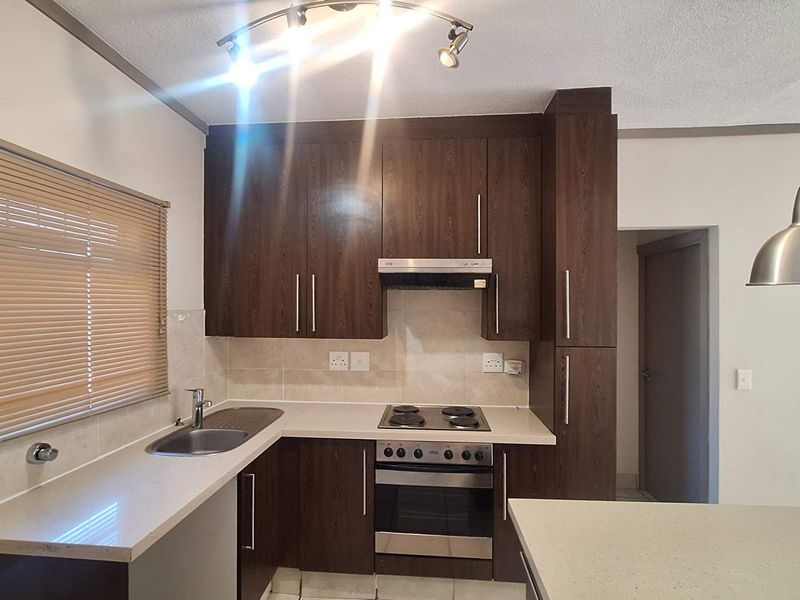 A functional kitchen featuring dark wood cabinetry, stone countertops, built-in oven with hob, extractor fan, and tiled backsplash.