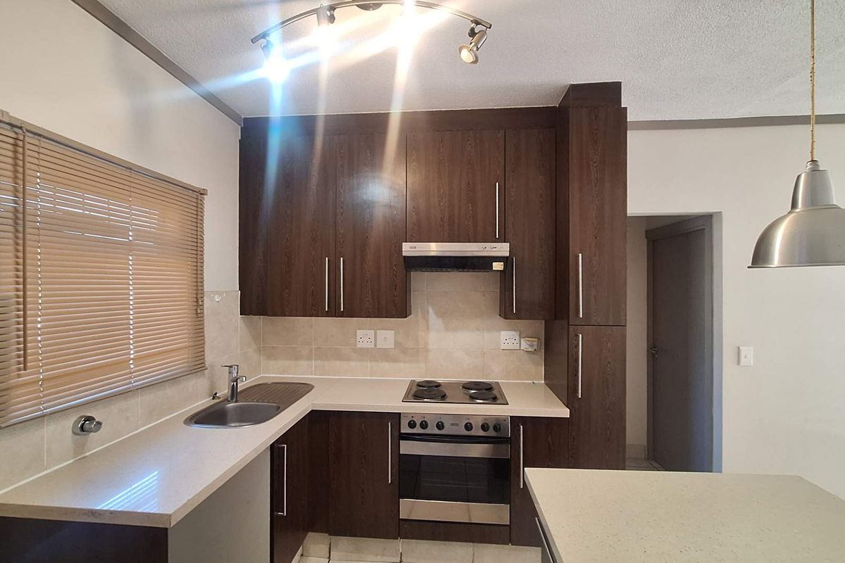A functional kitchen featuring dark wood cabinetry, stone countertops, built-in oven with hob, extractor fan, and tiled backsplash.