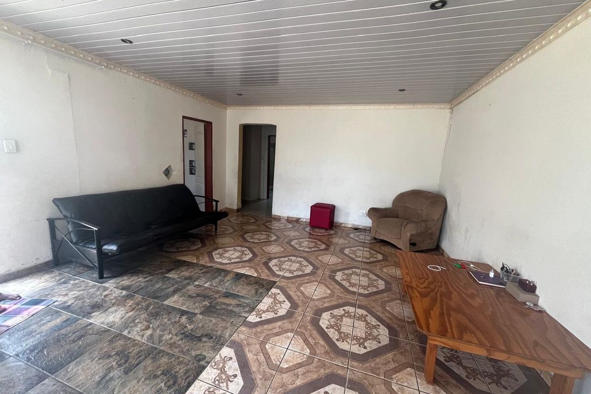 A living room featuring a coved ceiling with recessed lighting and mismatched tiled flooring, requiring cosmetic updates to improve the overall aesthetic.