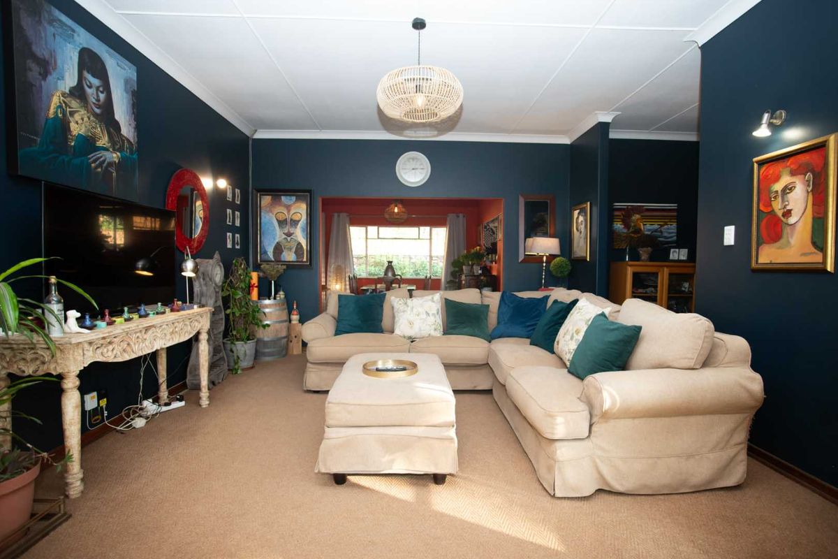 A spacious living room featuring dark blue walls, neutral carpeting, and decorative coving, with an open transition to an adjacent dining area.
