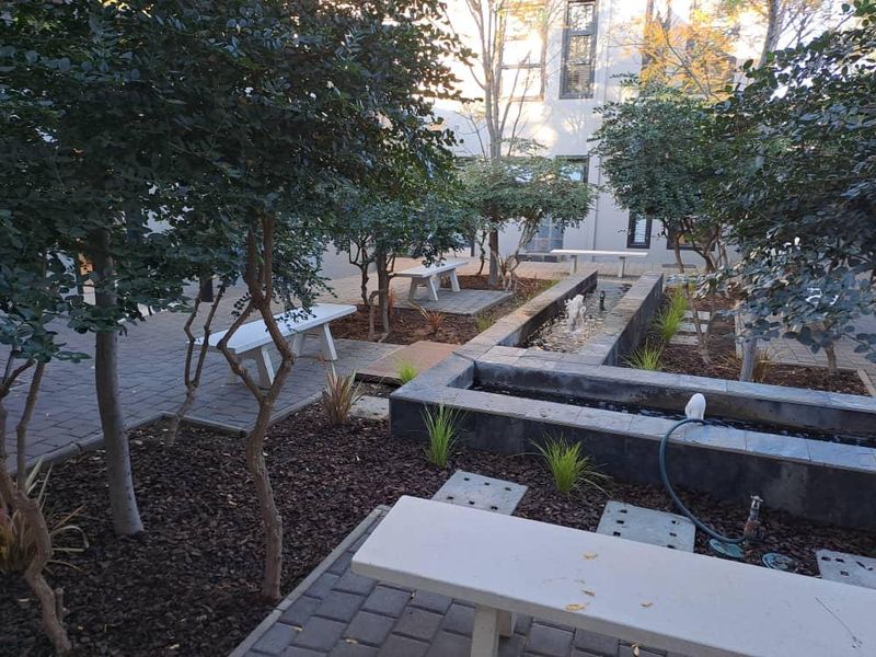 A well-maintained office courtyard garden featuring a central water feature, paved pathways, and built-in stone seating areas.