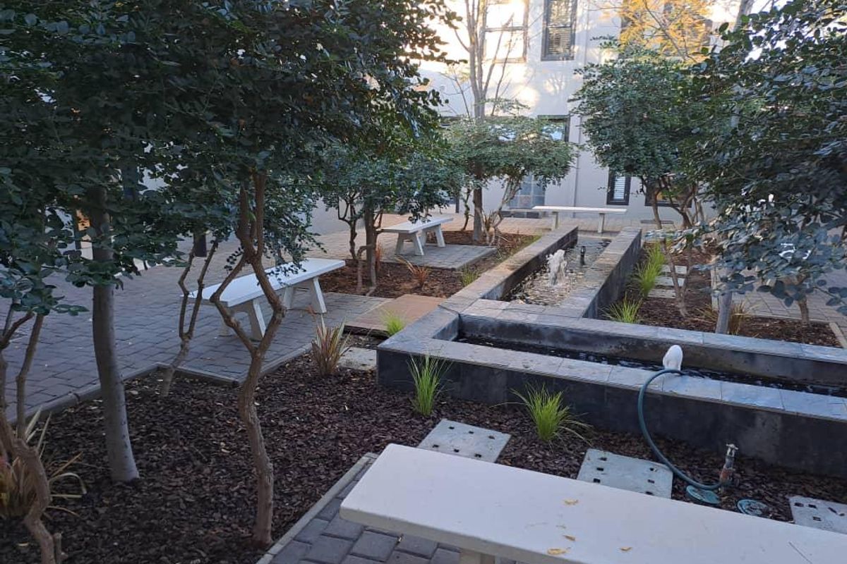A well-maintained office courtyard garden featuring a central water feature, paved pathways, and built-in stone seating areas.