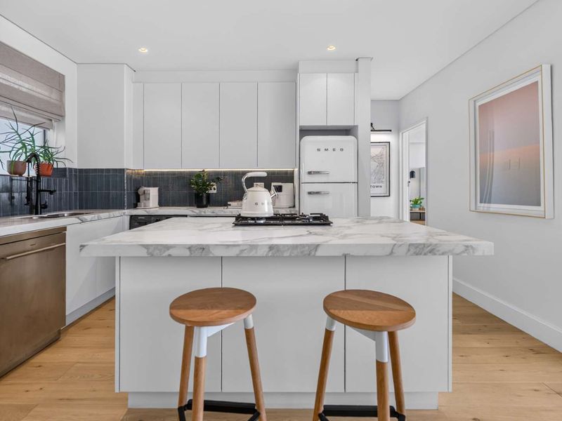 Modern kitchen featuring a marble-topped island, gas cooktop, integrated dishwasher, sleek white cabinetry, and high-quality hardwood flooring.