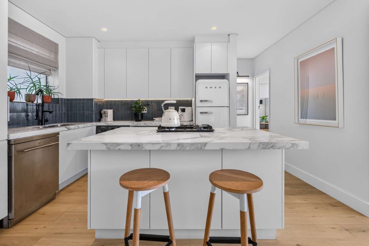 Modern kitchen featuring a marble-topped island, gas cooktop, integrated dishwasher, sleek white cabinetry, and high-quality hardwood flooring.
