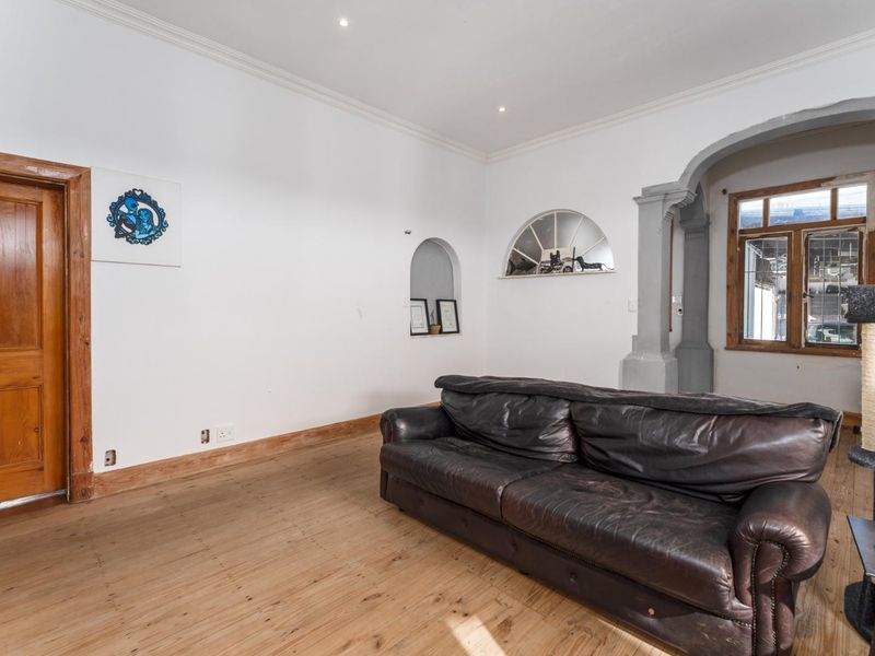 Living room featuring timber flooring, a decorative archway, and a recessed alcove, offering a character-filled space with potential for cosmetic updates.