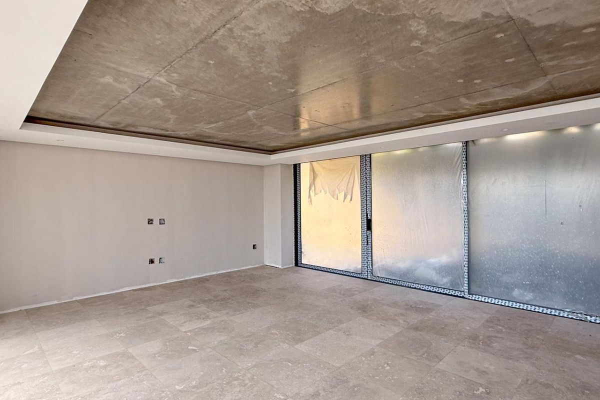 A spacious, modern living area featuring a raw concrete ceiling, large format floor tiles, and expansive sliding glass doors leading to an outdoor space.