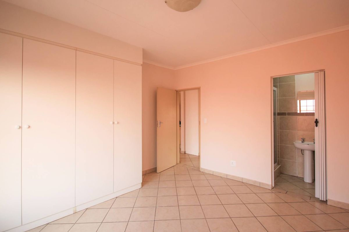 A bedroom featuring built-in cupboards, tiled flooring, and an en-suite bathroom with a pedestal basin and shower.