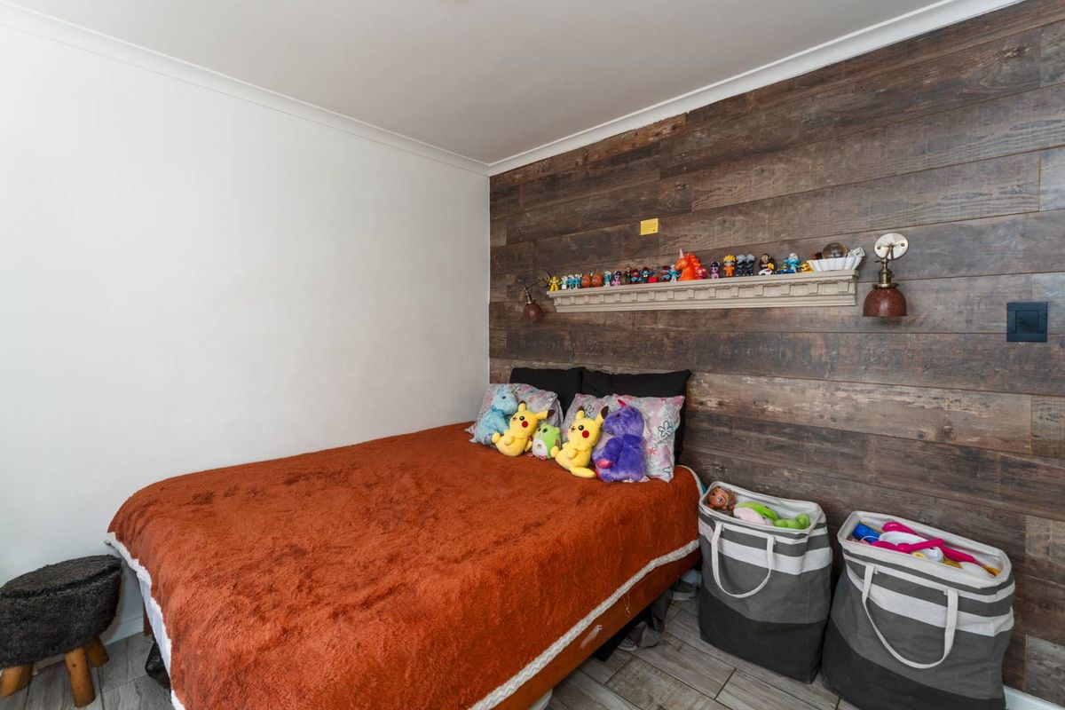 A bedroom featuring a rustic wood-paneled accent wall, built-in shelving, and wall-mounted lighting fixtures with tiled flooring.
