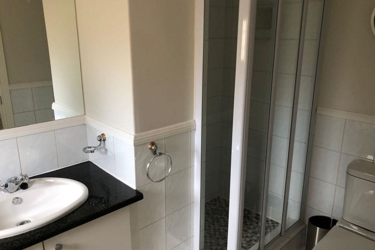 A functional bathroom featuring a shower enclosure, vanity basin with granite countertop, and a toilet, finished with tiled splashbacks.