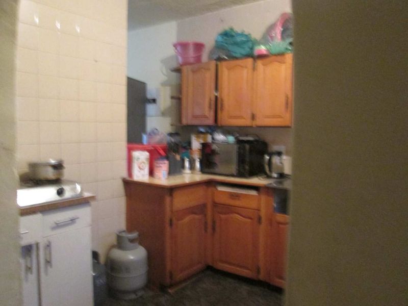 A compact kitchen featuring dated wooden cabinetry, tiled backsplash, and a gas stove setup, offering potential for a modern renovation.