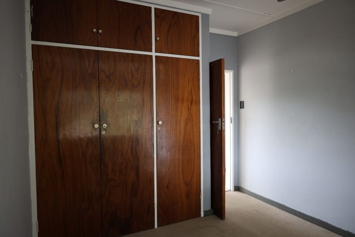 A vacant bedroom featuring built-in wooden cupboards and carpeted flooring, offering a blank canvas for potential updates and interior design.