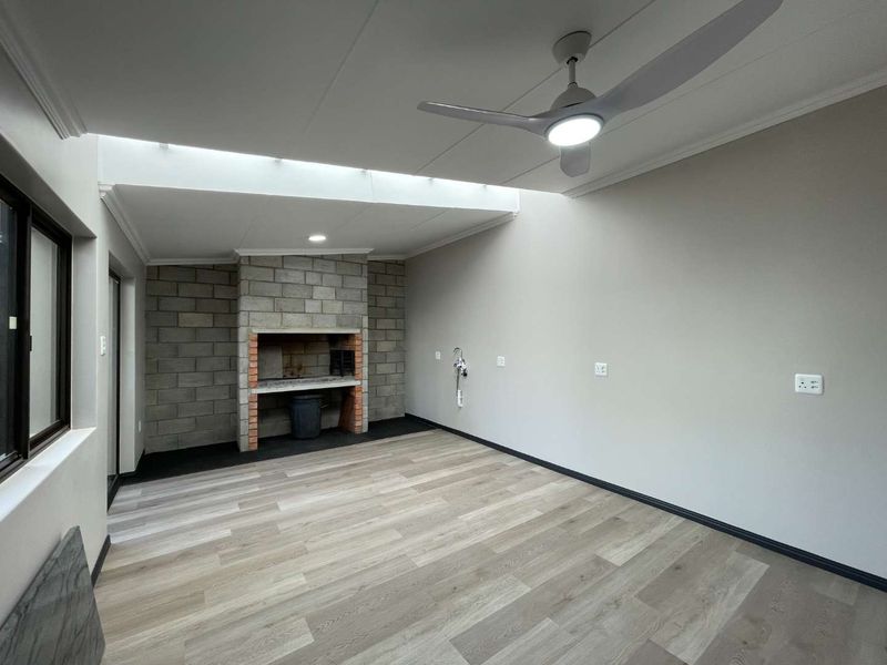 A clean, modern enclosed patio featuring a built-in braai, laminate flooring, a skylight, and a ceiling fan, offering a versatile entertainment space.