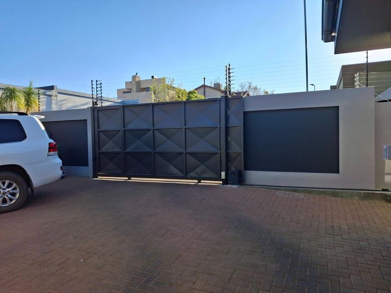 A secure front entrance featuring a modern black sliding gate, perimeter walling with integrated electric fencing, and a paved driveway.