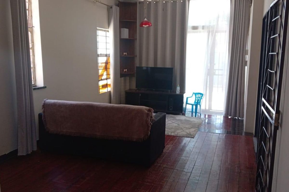 A living room featuring dark timber flooring, built-in corner shelving, and large windows providing natural light with access to an outdoor area.