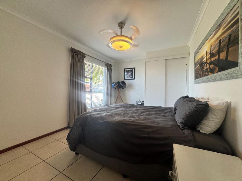 A bedroom featuring tiled flooring, a built-in wardrobe, and a ceiling fan, offering a functional and well-lit space.