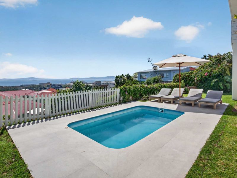 A well-maintained swimming pool area featuring a paved deck, picket fencing, and expansive coastal views.