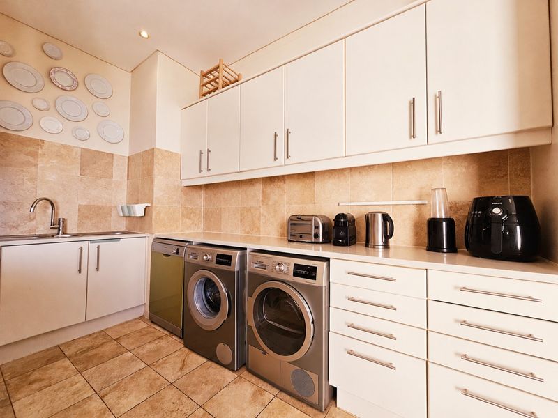 A well-appointed scullery featuring ample built-in cabinetry, stone countertops, tiled backsplash, and dedicated space for laundry appliances and a sink.