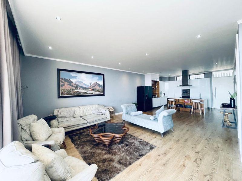 Spacious open-plan living area featuring modern laminate flooring, recessed lighting, and a contemporary kitchen with a central island and integrated appliances.