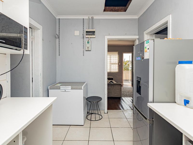 Functional scullery area featuring tiled flooring, built-in cabinetry, and direct access to the living space, requiring cosmetic updates to improve overall finish.