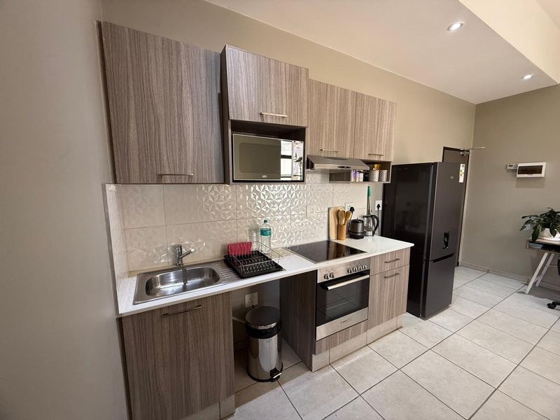 Modern kitchen featuring wood-grain cabinetry, integrated appliances including an oven and hob, a tiled backsplash, and neutral floor tiles.