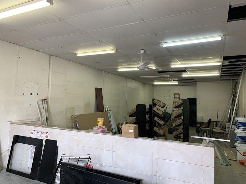 Vacant retail utility space featuring a suspended ceiling, tiled partition wall, and basic fluorescent lighting, currently in need of refurbishment.
