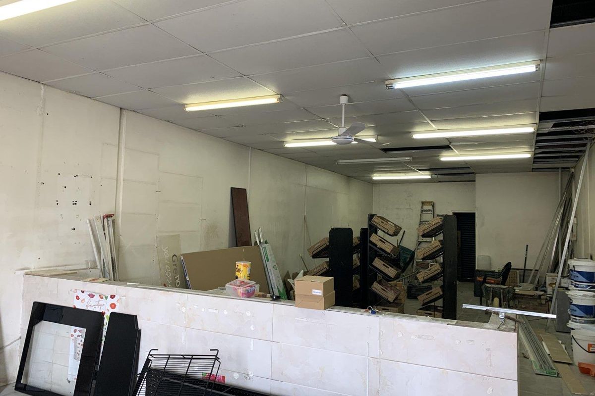 Vacant retail utility space featuring a suspended ceiling, tiled partition wall, and basic fluorescent lighting, currently in need of refurbishment.