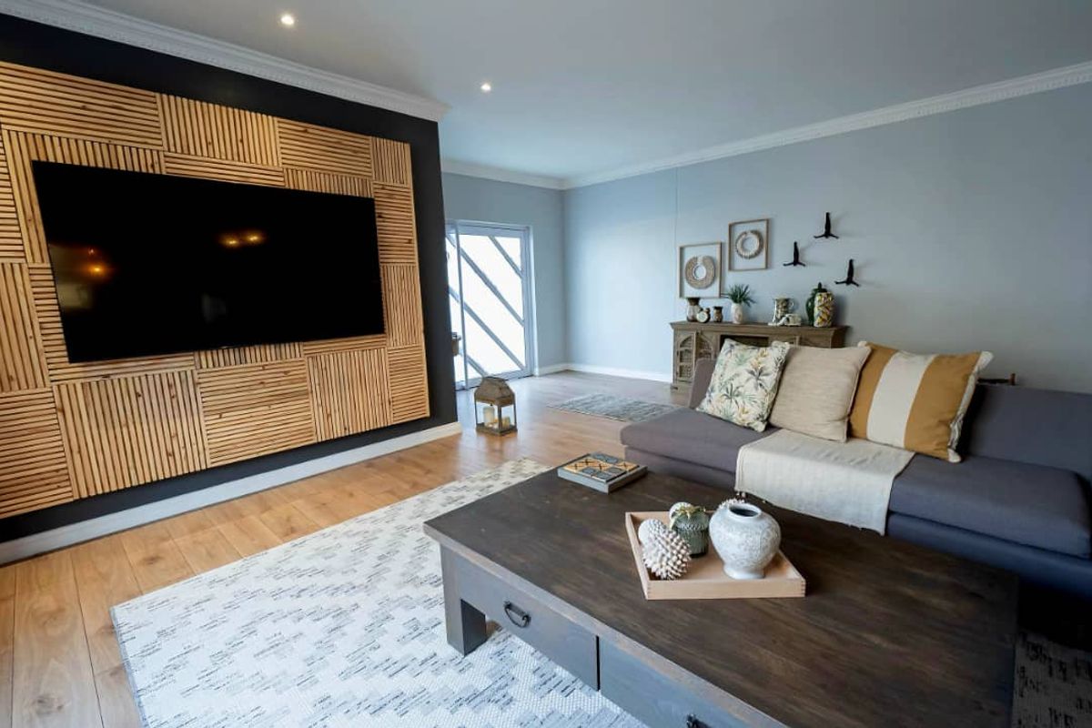 Spacious living room featuring light wood flooring, recessed ceiling lighting, and a decorative timber-slatted feature wall with a mounted television.